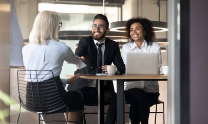 Multi-ethnic business partners greet each other shake hands sit at desk in modern office room, Arabian HR manager handshake welcoming applicant elderly female rear view starting job interview concept