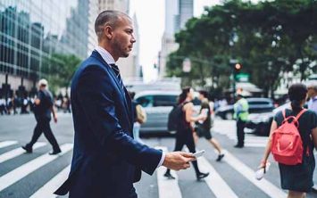 Side view of confident businessman passing crosswalk in modern district of megalopolis choosing direction, serious male entrepreneur crossing street with crowd getting to office building by foot